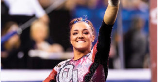 Maggie Nichols smiles and holds her left arm aloft, pointing one finger at something off camera in celebration.